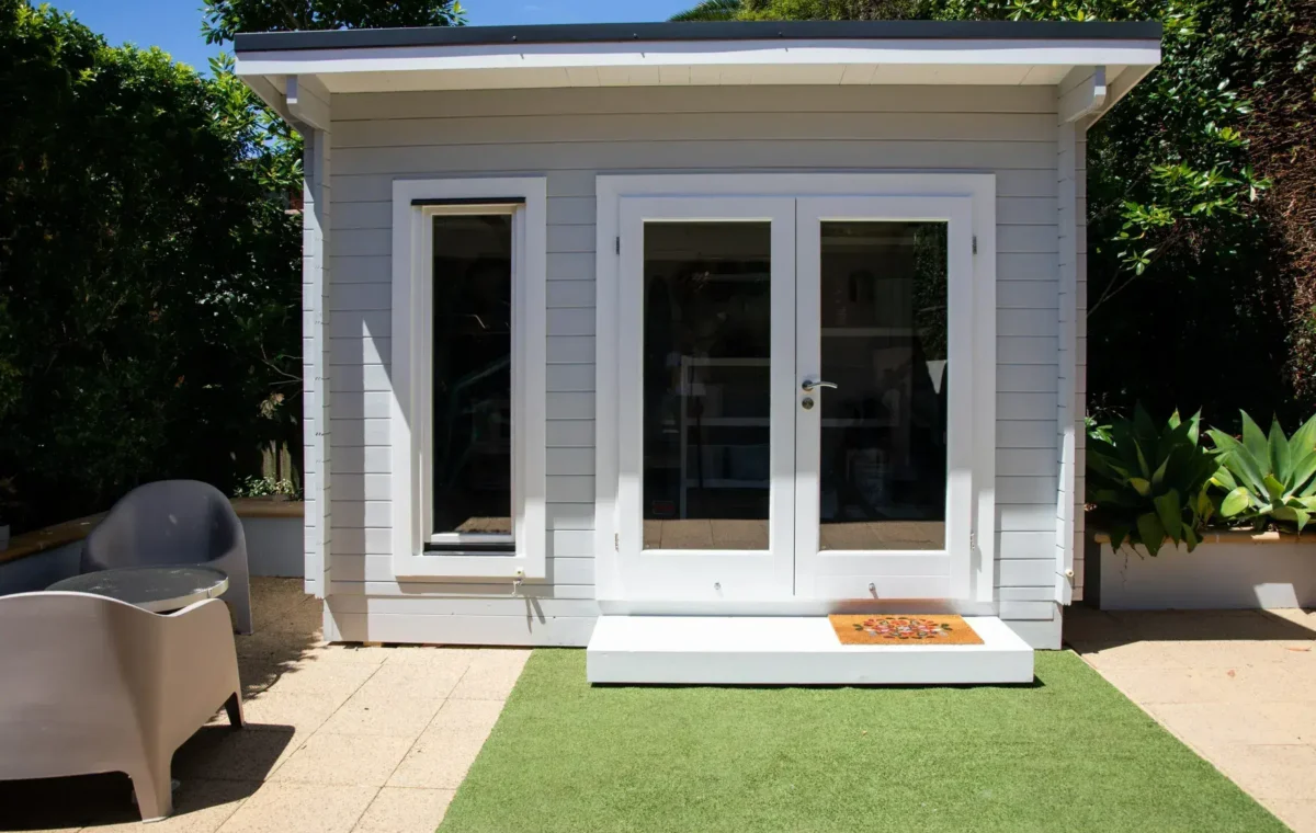 Modern gray garden house with white framed glass doors and small patio area