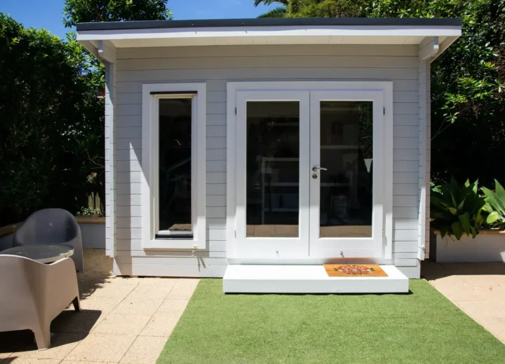 Modern gray garden house with white framed glass doors and small patio area